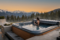 A high-end outdoor spa featuring a woman seen from behind, enjoying a drink while looking out at a panoramic view of snow-capped mountains and fir trees at sunset. The hot tub cover is partially folded to the side. 