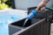 Close-up of a garden hose fitted with a transparent blue pre-filter inserted into the filtration compartment of an outdoor hot tub for filling it with pure water.